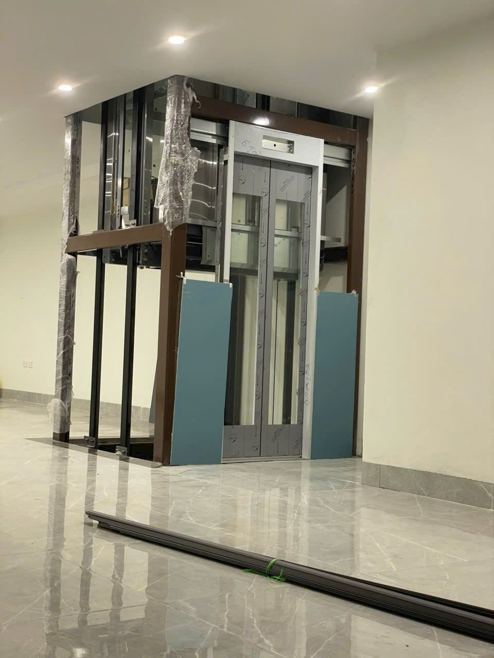 Thang máy gia đình đang lắp đặt dở trong nhà với khung kim loại và cửa tầng chưa hoàn thiện